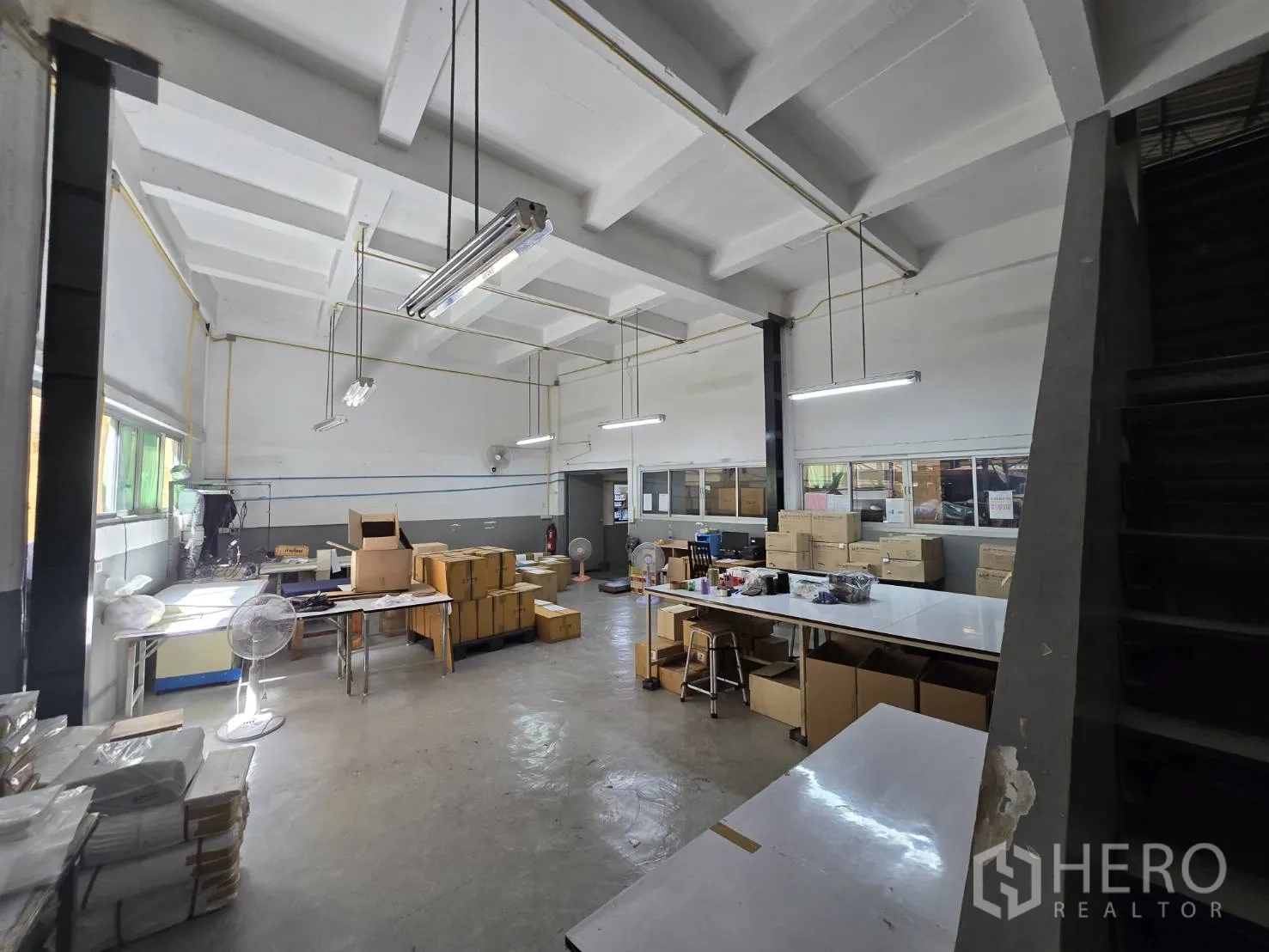 Factory for rent in Sam Phran, Nakhon Pathom - Bright packing workspace with high ceiling, tables, and boxed inventory.