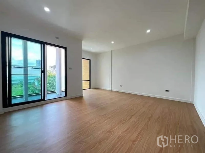 Townhouse for sale in Watthana, Bangkok - Sunlit bedroom with wood floors and two balconies accessed by sliding doors.