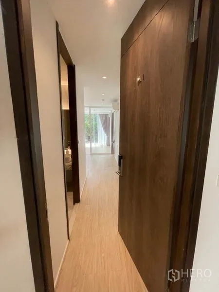 Home Office for rent in Khlong Toei, Bangkok - Entrance hallway with wooden door and recessed lights leading toward a bright glass-partitioned room.