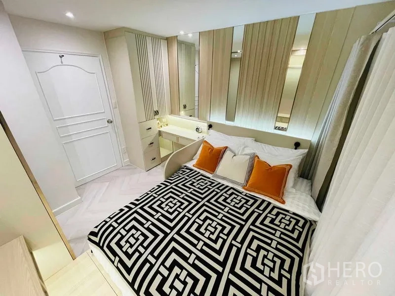 Condominium for sale in Yan Nawa, Bangkok - Cozy bedroom with patterned black-and-white duvet, orange pillows, and built-in vanity.