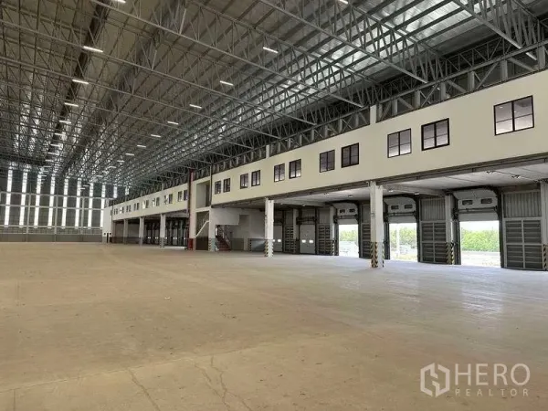 工厂 出租或出售在Samut Prakan - 超大仓库内景，高钢结构屋顶、夹层办公室与多组卷帘门。