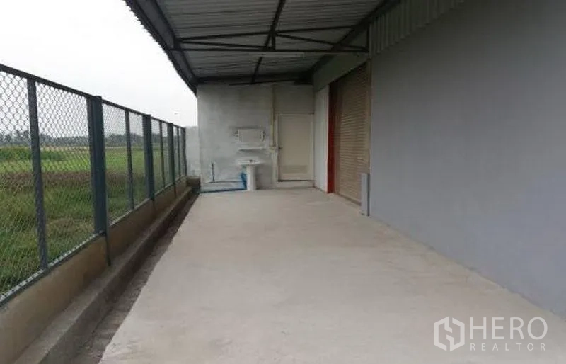 工厂 出租在Pathum Thani - 后侧有顶服务区，设水槽、卷帘门与围栏通道。