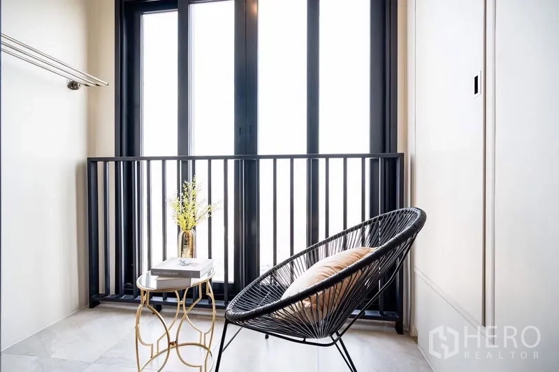 Condominium for rent in Watthana, Bangkok - Compact balcony or loggia with black-framed doors, lounge chair and side table.