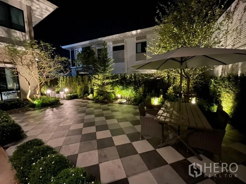 Detached House for rent in Phasi Charoen, Bangkok - Night view of garden patio with umbrella seating and ambient lighting.