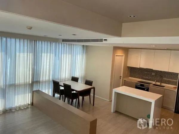 Condominium for sale in Watthana, Bangkok - Elevated view of open-plan kitchen and dining area framed by full-height sheer curtains.