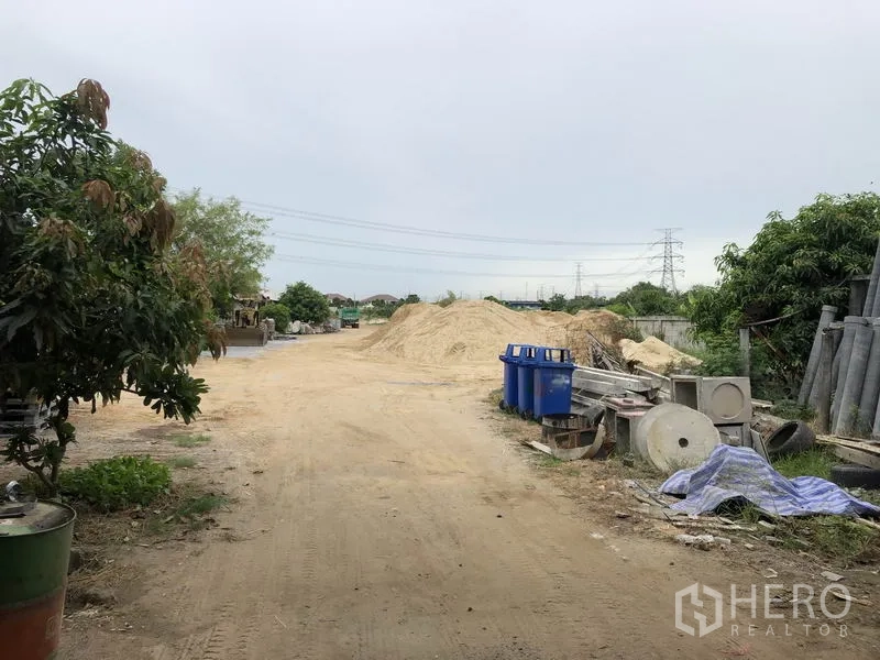 คลังสินค้า ให้เช่าในSai Noi, Nonthaburi - ลานเก็บกลางแจ้งกองทราย ถังสีน้ำเงิน ท่อคอนกรีต และเสาไฟฟ้าไกลๆ