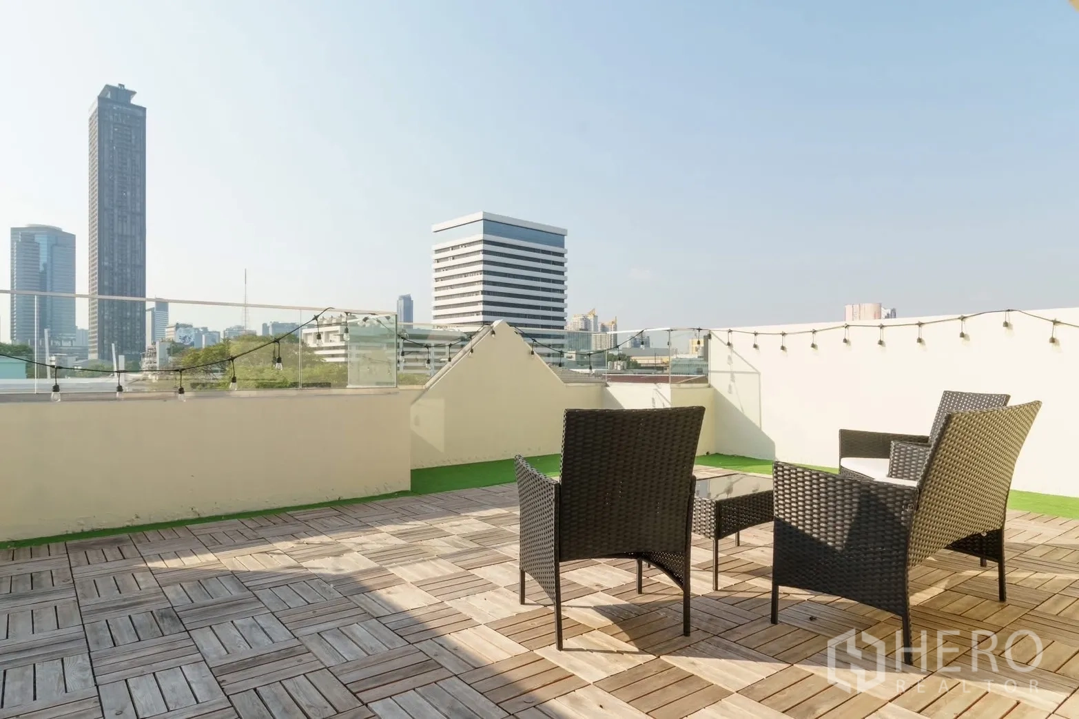 联排别墅 for rent in Watthana, Bangkok - 屋顶露台配藤编座椅与木地台，远眺城市天际线。