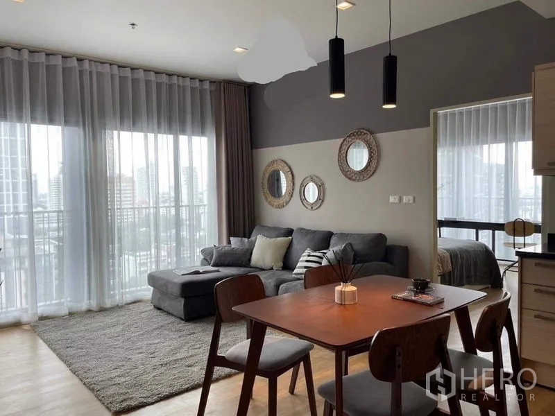 คอนโด ให้เช่าในWatthana, Bangkok - ห้องนั่งเล่นและรับประทานอาหารแบบโอเพ่น พร้อมหน้าต่างสูงจรดเพดาน โซฟาเข้ามุม และระเบียงวิวเมือง