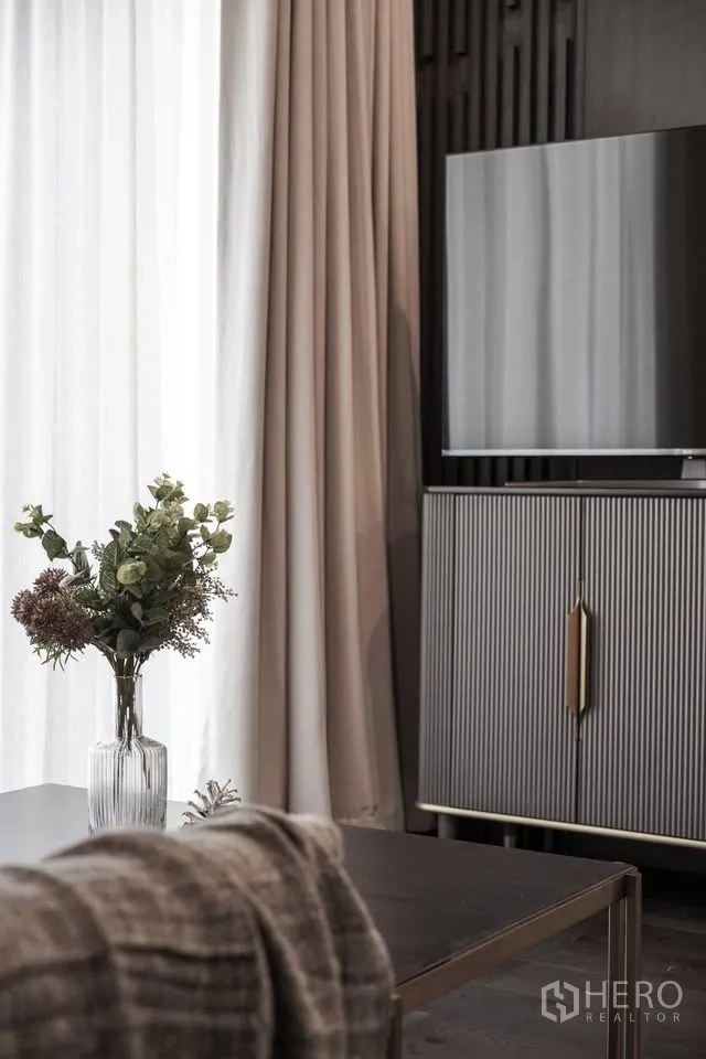 Condominium for rent in Watthana, Bangkok - Living room corner with TV console, full-height curtains, and a vase on the coffee table.