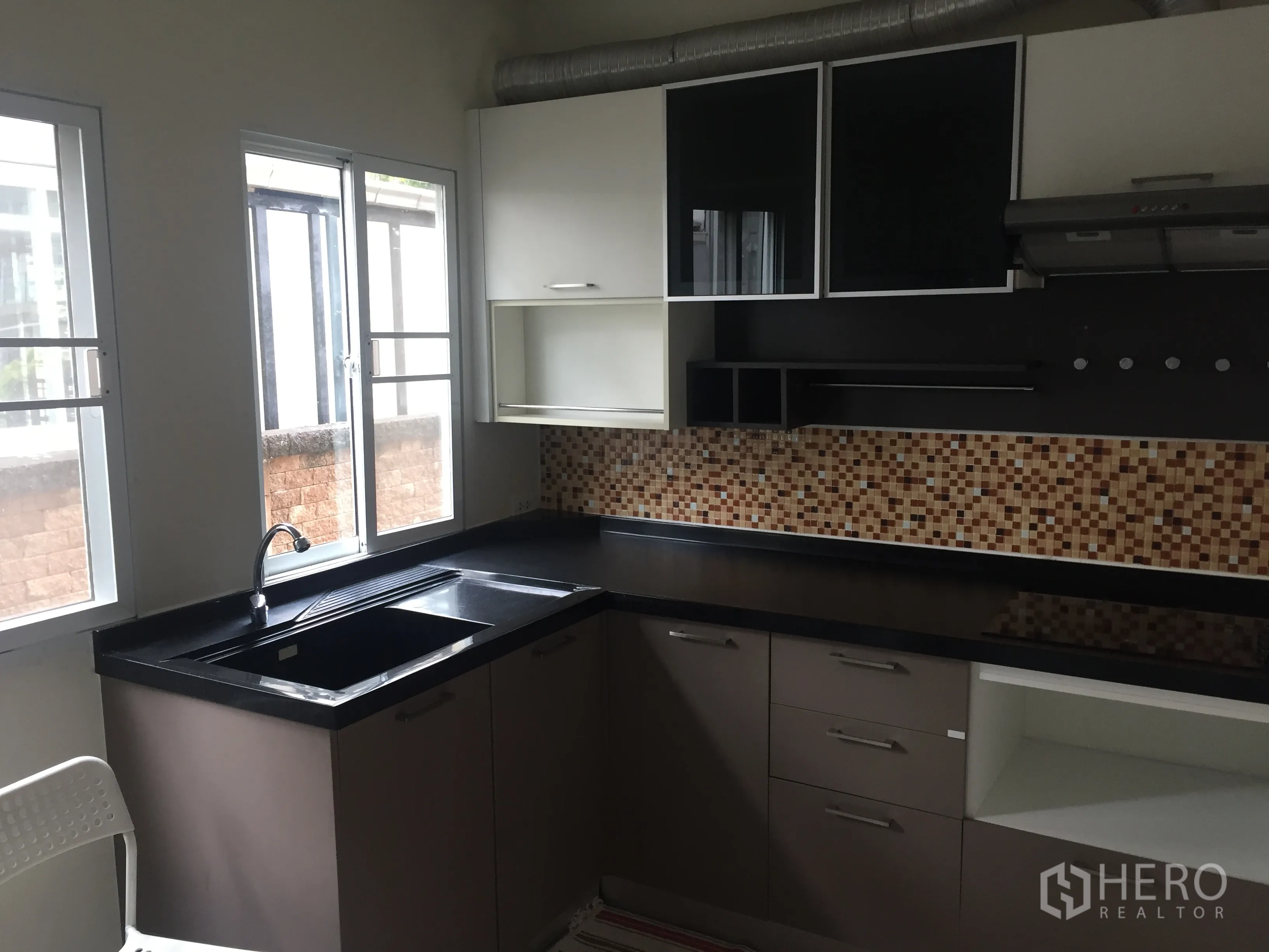 Detached House for rent in Pathum Thani - Fitted kitchen with black countertops, mosaic backsplash, upper cabinets, windows and range hood.