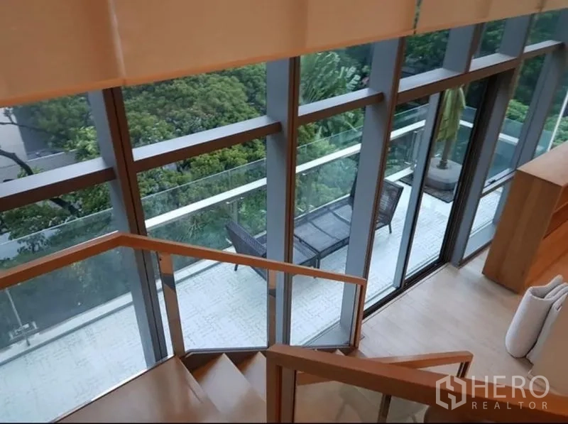 Condominium for rent or sale in Watthana, Bangkok - Long balcony along a glass facade viewed from the stairs, featuring outdoor seating and leafy outlook.