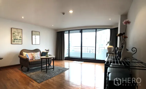 คอนโด ให้เช่าในKhlong Toei, Bangkok - ห้องนั่งเล่นกว้าง เปิดสู่ระเบียงกระจกโค้งพร้อมวิวเมืองและโซฟาหวาย