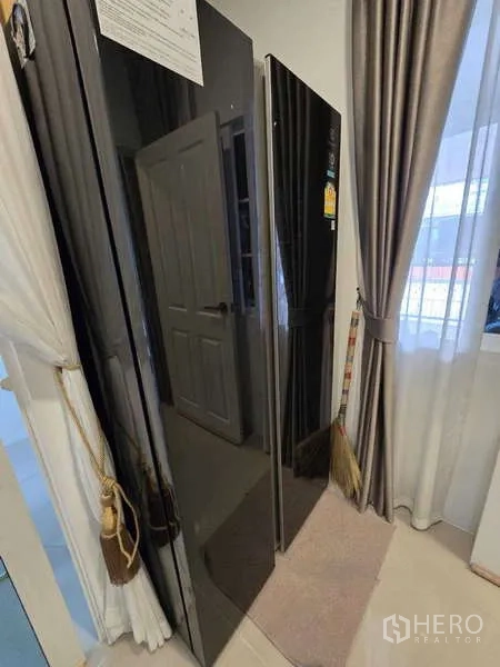 Detached House for rent in Thanyaburi, Pathum Thani - Tall black refrigerator and storage area beside large curtained windows.