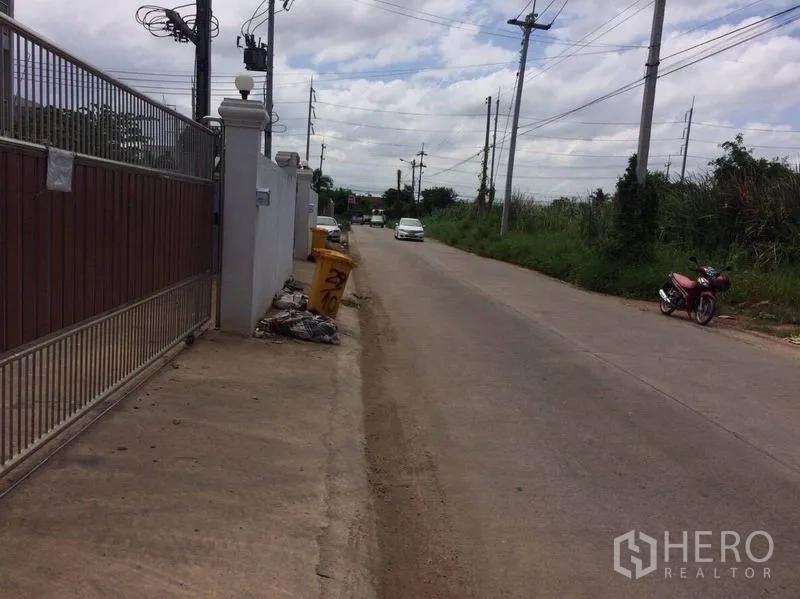 Factory for rent or sale in Mueang Samut Sakhon, Samut Sakhon - Quiet access road beside the property gate with power lines and light traffic.