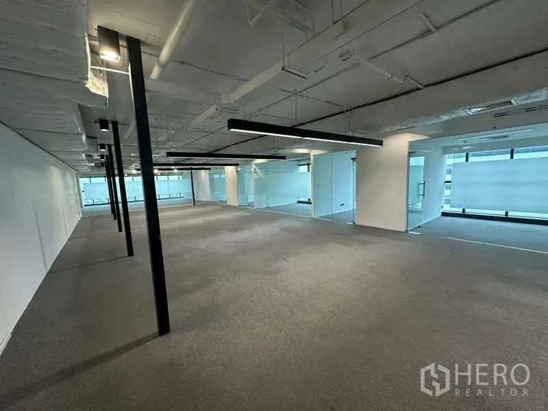 Office Space for rent - Expansive open office area with suspended linear lights and glass partitions.