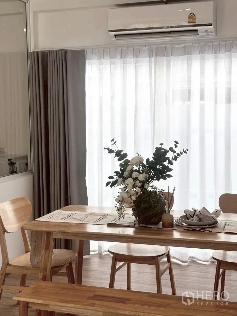 Townhouse for rent in Prawet, Bangkok - Dining area with wooden table, chairs and floral centerpiece under a wall-mounted AC.