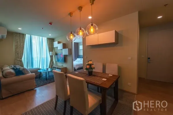 Condominium for rent in Watthana, Bangkok - Open-plan living and dining area with warm pendant lights, wall-mounted TV and sofa.