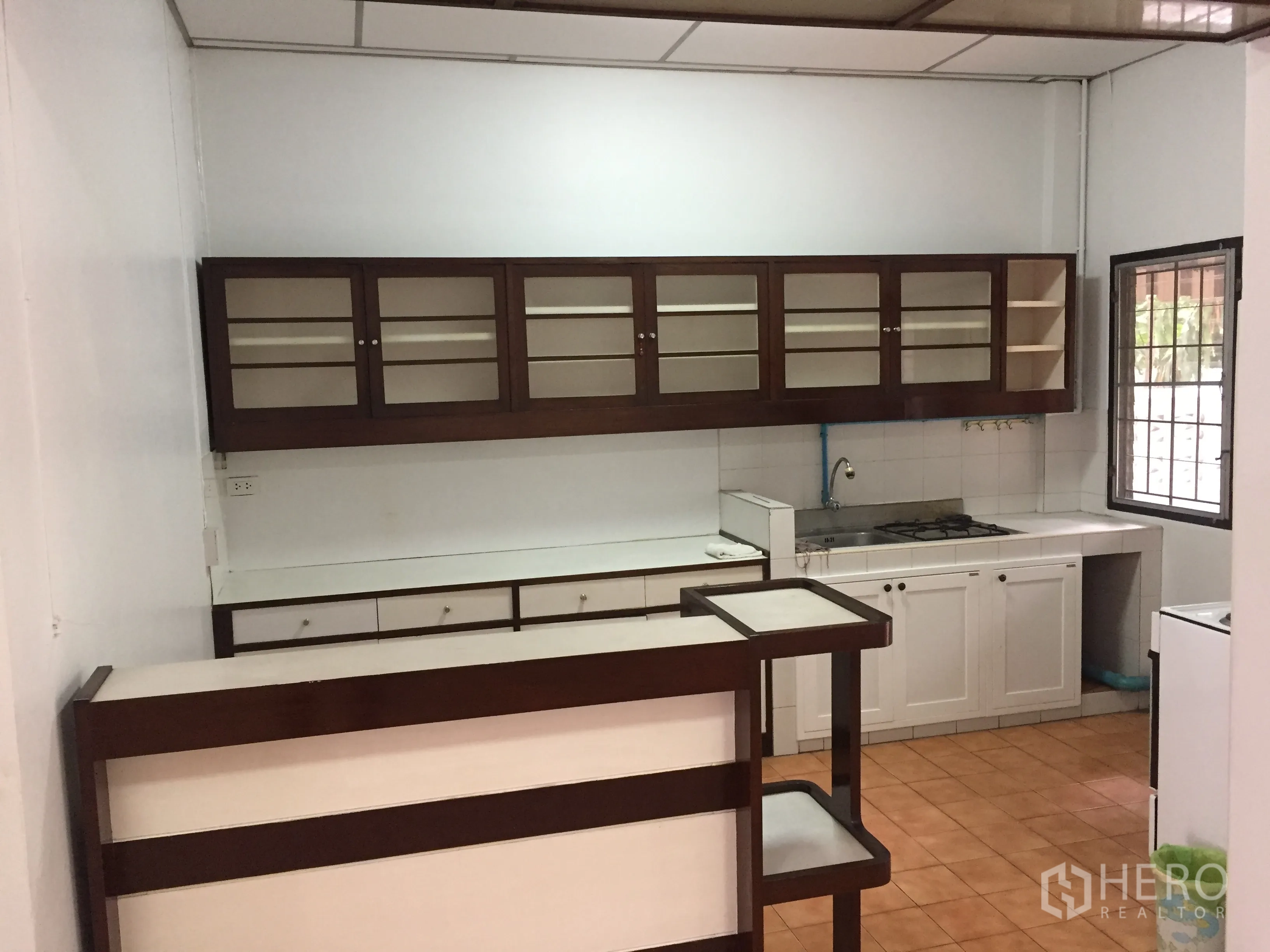 Townhouse for rent in Khlong Toei, Bangkok - Townhouse kitchen with white counters, gas hob, and glass-front upper cabinets in Watthana, Bangkok.