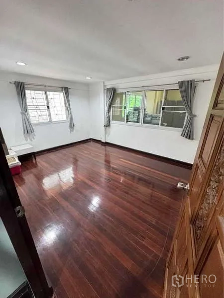 Detached House for rent in Suan Luang, Bangkok - Bright bedroom with glossy wooden floor and two windows with curtains.