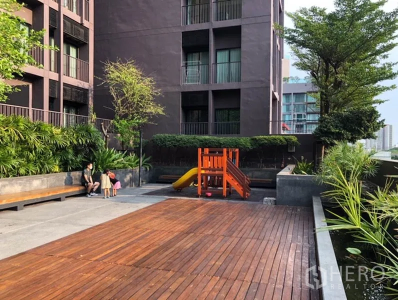 Condominium for rent or sale in Watthana, Bangkok - Condo courtyard with wooden deck, landscaped greenery, and a children’s play set.