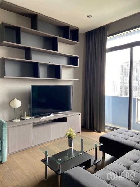 Condominium for sale in Bang Rak, Bangkok - Living area with TV wall, open shelves and sliding doors to a balcony.
