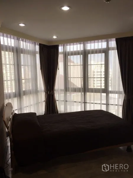 Condominium for rent in Watthana, Bangkok - Corner bedroom with floor-to-ceiling windows, sheer curtains and urban outlook.