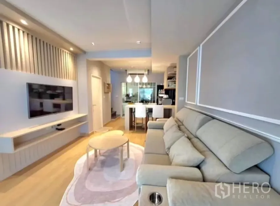 Townhouse for rent in Bang Phli, Samut Prakan - Bright living room with built-in TV wall, large sofa and open-plan dining in Bang Phli townhouse.
