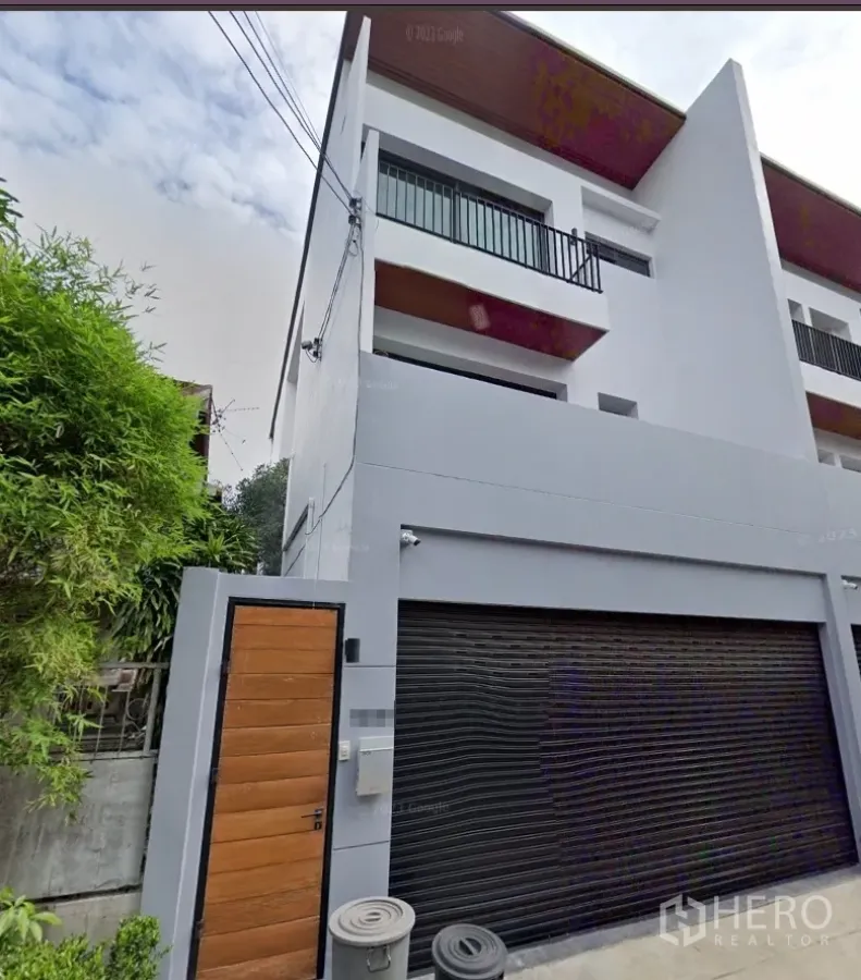 联排别墅 出租在Watthana, Bangkok - 现代三层联排别墅外立面，黑色卷闸车库与木门。