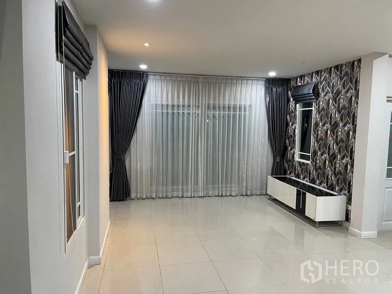 Detached House for rent in Bang Kapi, Bangkok - Spacious living area with floor-to-ceiling curtains, feature wallpaper and tiled flooring.