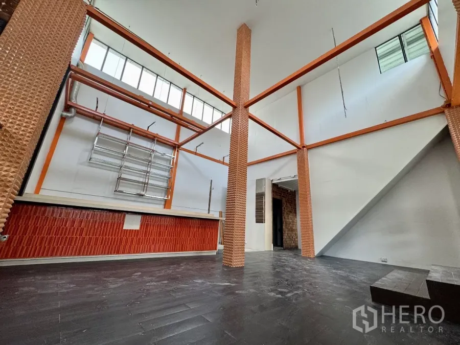 Shophouse for rent in Sathon, Bangkok - Double-height retail hall with orange steel beams, dark flooring and a service counter.