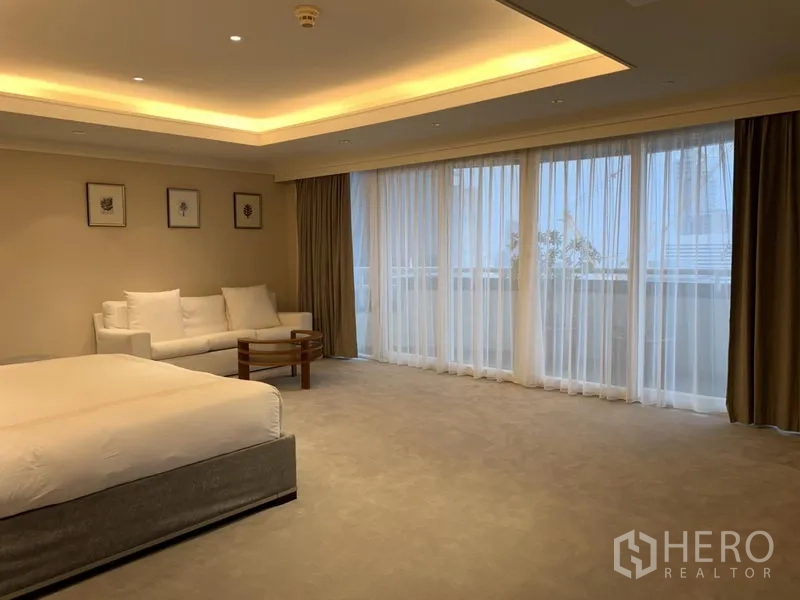 Condominium for rent or sale in Watthana, Bangkok - Oversized bedroom with carpeted floor, sofa corner and sheer curtains to balcony.