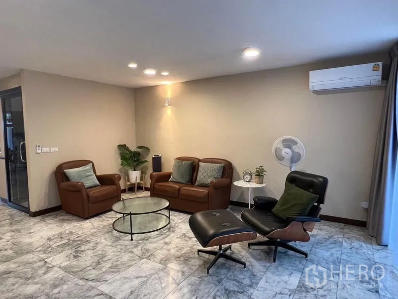 Townhouse for sale in Suan Luang, Bangkok - Living room with leather sofas, lounge chair, glass coffee table and marble flooring.