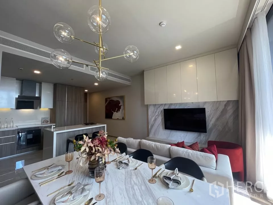 Condominium for rent in Watthana, Bangkok - Marble dining table set for six beside the open kitchen and TV wall with stone cladding.