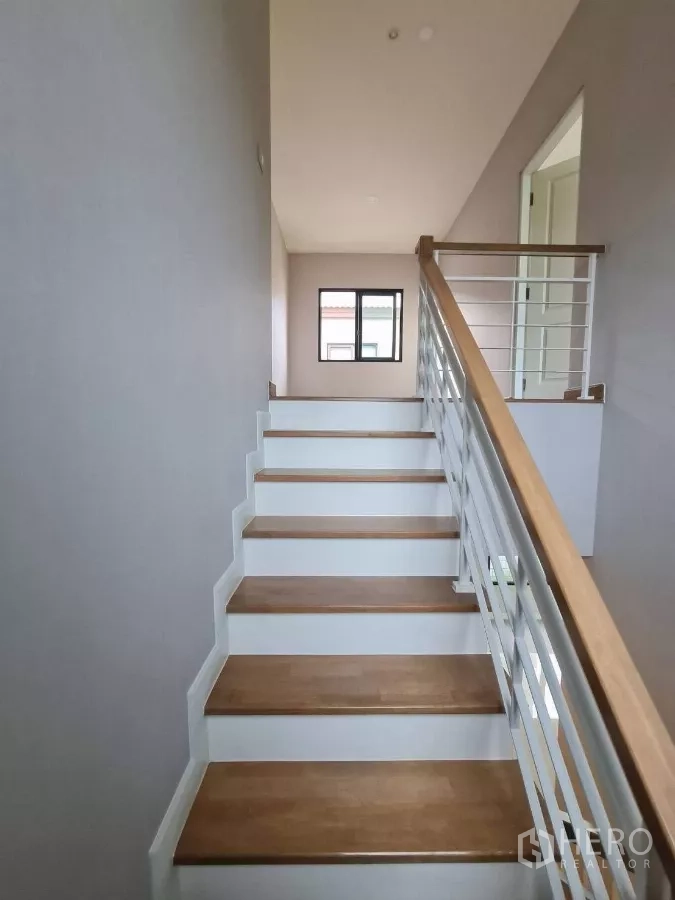Detached House for sale in Samut Prakan - Staircase with wooden treads, white handrail and window bringing in natural light.