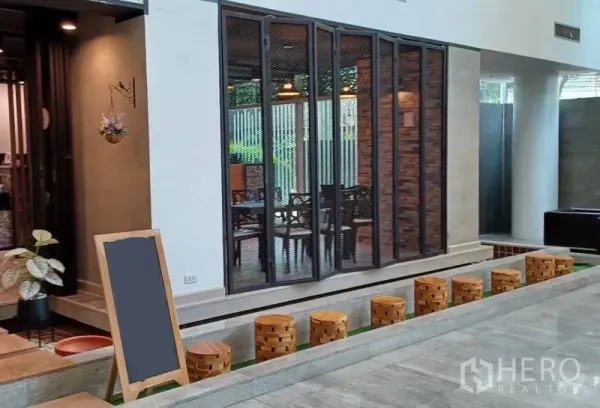 零售空间 出租在Khlong Toei, Bangkok - 现代零售店铺门面，折叠玻璃门与砖纹墙面，步道旁摆放木质圆凳。