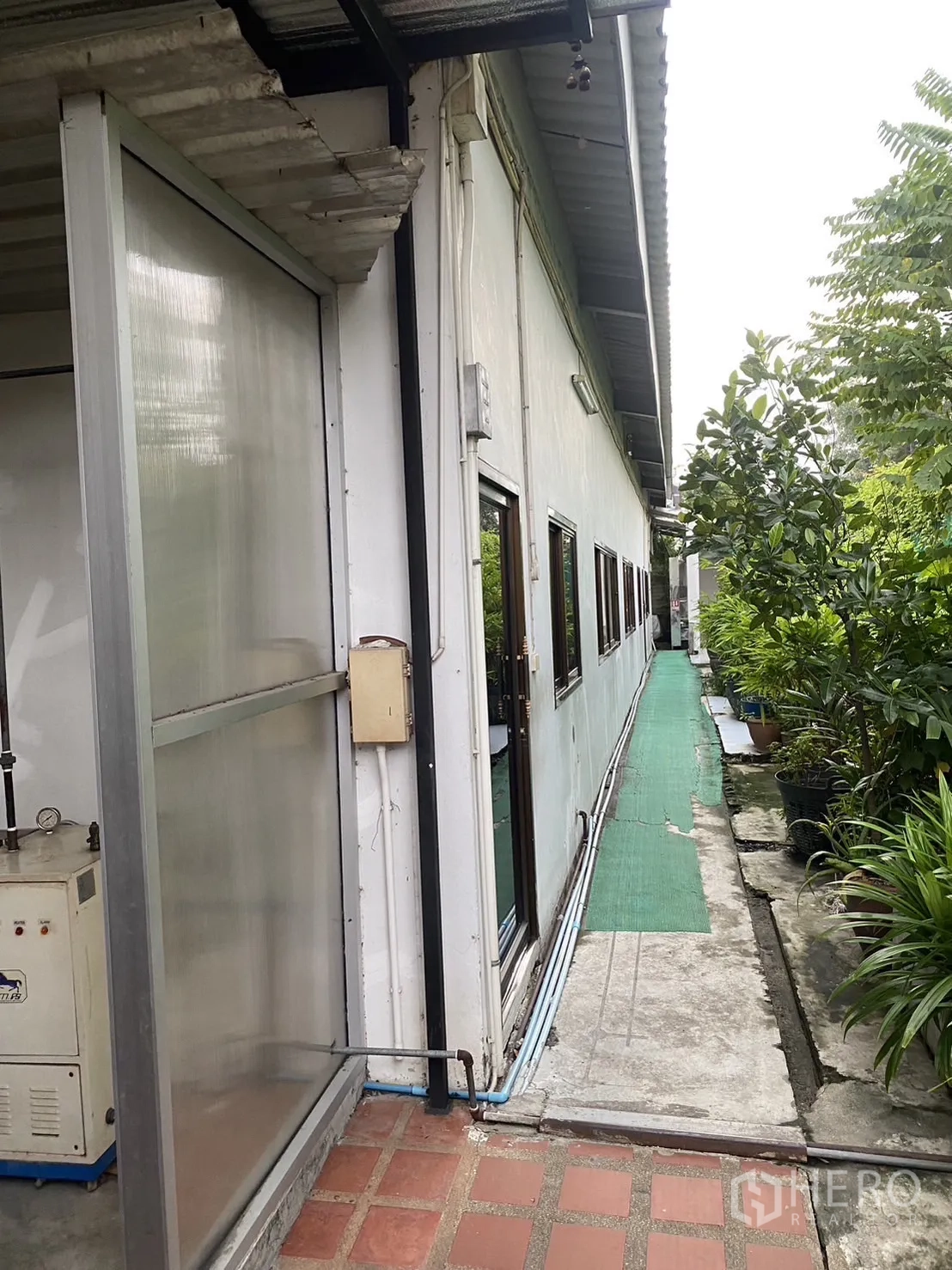 工厂 出租在Prawet, Bangkok - 建筑侧方服务走道，铺设绿色地垫并配有植被