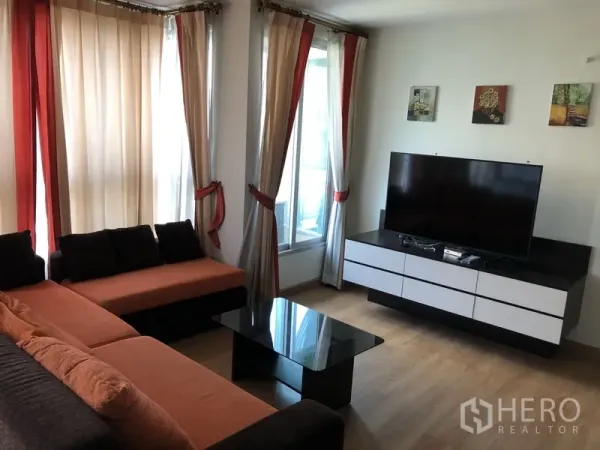 Condominium for rent in Khlong Toei, Bangkok - TV lounge with large flat-screen, media console, coffee table, and corner windows.
