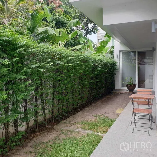 Detached House for rent in Watthana, Bangkok - Shaded side garden with trimmed hedge, narrow path, outdoor bistro set and sliding door entry.