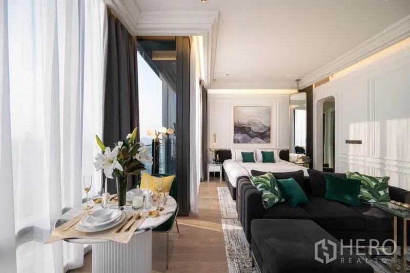 Condominium for rent in Bang Rak, Bangkok - Open-plan suite with dining table, sofa and king bed framed by tall windows and soft drapes.