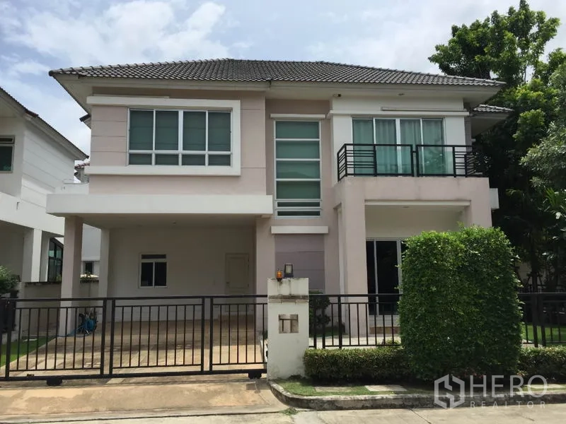 Detached House for rent or sale in Saphan Sung, Bangkok - Two-storey detached house facade with gated carport, balcony and landscaped hedge in a quiet community.
