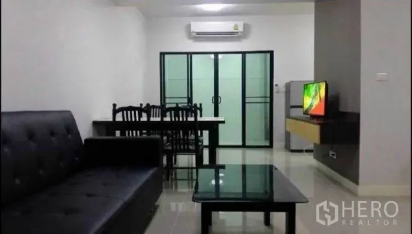 Townhouse for rent in Suan Luang, Bangkok - Living room with black sofa, glass coffee table, dining table, air conditioner and sliding glass doors.