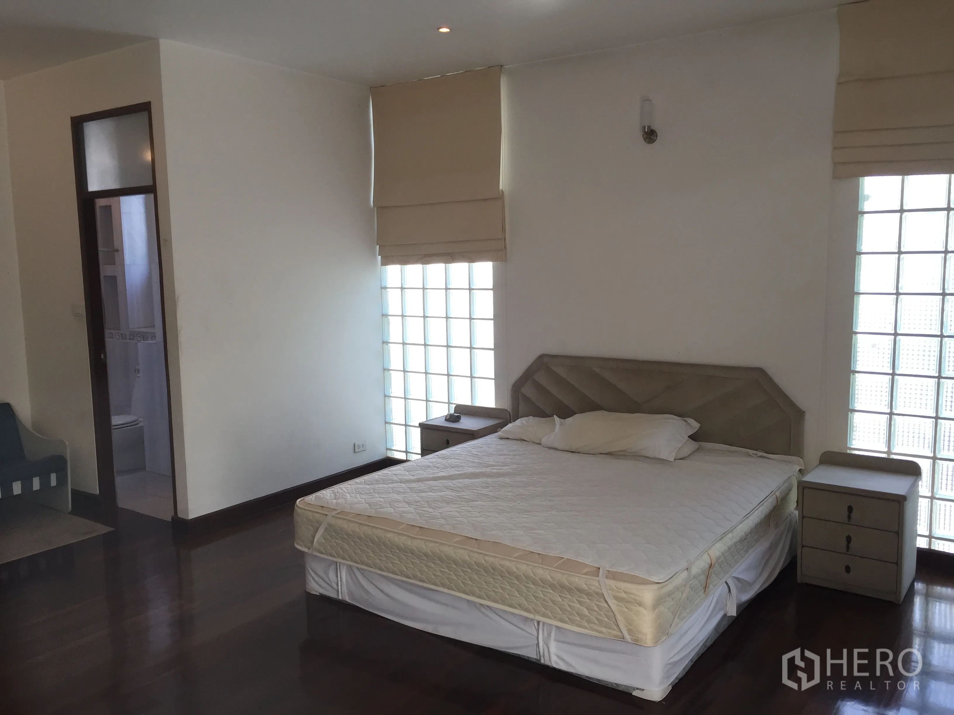 Condominium for rent in Watthana, Bangkok - Bright bedroom featuring a king bed, glass-block windows, bedside tables and a door to the ensuite bathroom.