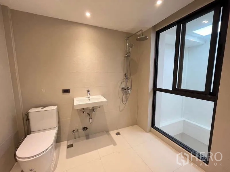 Townhouse for sale in Khlong Toei, Bangkok - Large neutral bathroom with window, rain shower, toilet and sink.