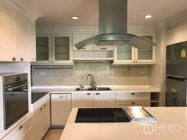 Condominium for rent in Sathon, Bangkok - White U-shaped kitchen with island cooktop, range hood, built-in oven and ample cabinets.