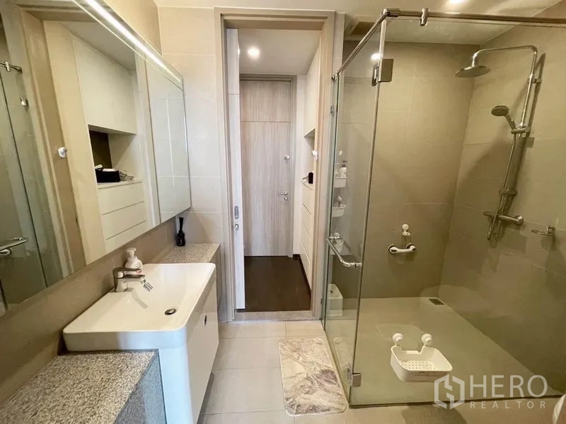 Condominium for rent in Pathum Wan, Bangkok - Bright bathroom featuring a glass-enclosed rain shower, vanity, and storage cabinets.