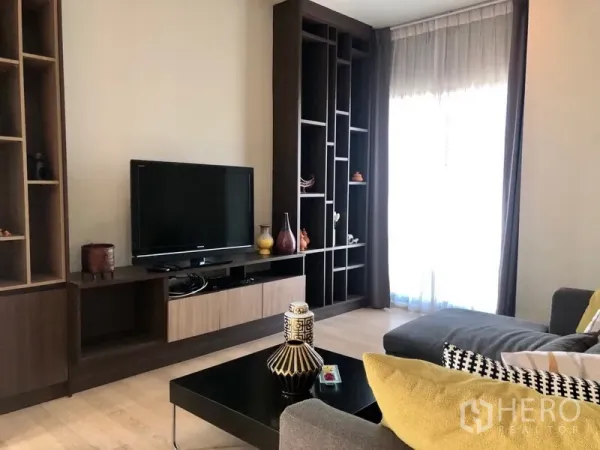 公寓 出租或出售在Bangkok - 电视背景墙配内置层架与柜体，旁为落地窗与纱帘。