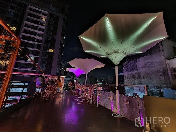 พื้นที่ขายปลีก ให้เช่า - โซนที่นั่งบนรูฟท็อปพร้อมร่มทรงประติมากรรม ไฟสีม่วง และฉากหลังสกายไลน์