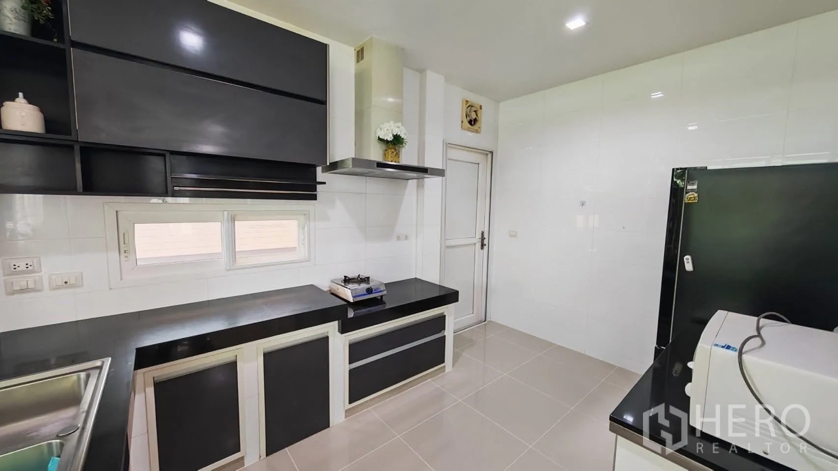 Detached House for rent or sale in Bang Phli, Samut Prakan - Contemporary kitchen featuring black countertops, glossy cabinetry, and a range hood.