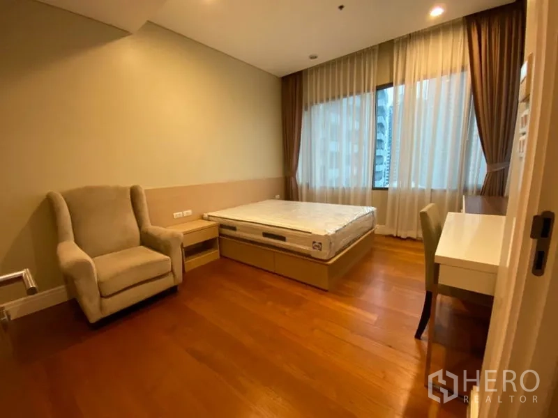 Condominium for rent in Khlong Toei, Bangkok - Second bedroom with armchair, bed base, study desk and floor-to-ceiling curtains.