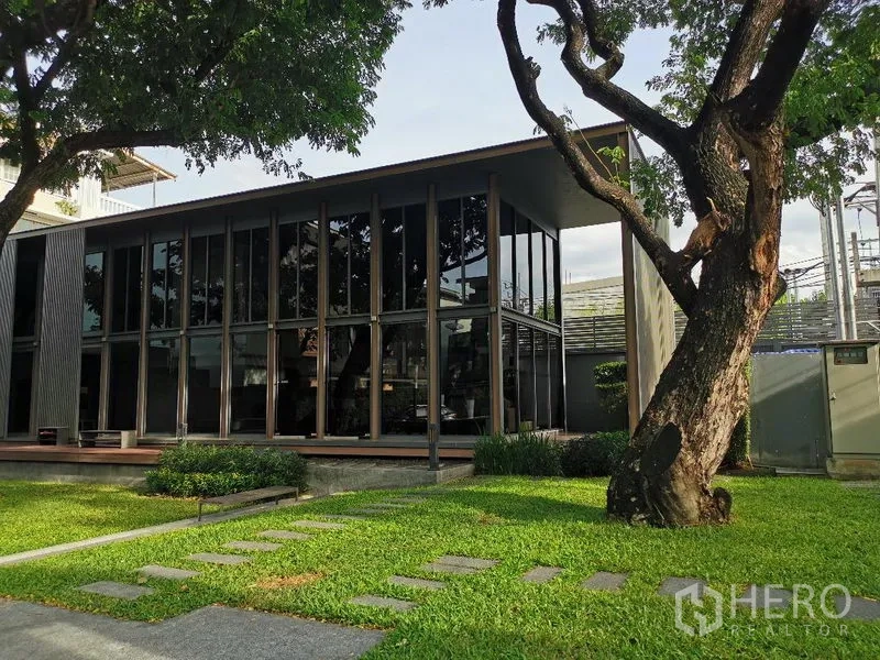 Detached House for sale in Wang Thonglang, Bangkok - Landscaped lawn with mature trees and a glass-walled community pavilion within the estate.